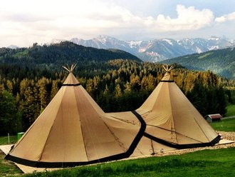 Ein 2er-Tipi ist von hinten fotografiert. Das Zelt steht in einer Berglandschaft. Das Bild hat einen Retro-Vibe.