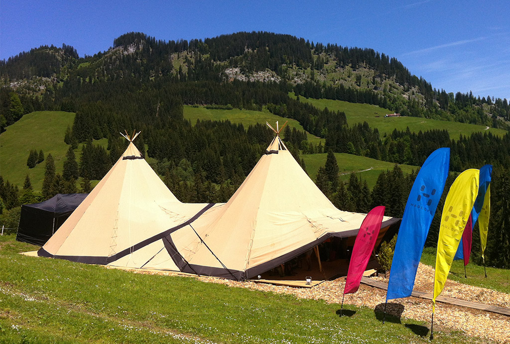 Ein Zweier-Tipi steht mit bunten Beachflags in einer Hügellandschaft.